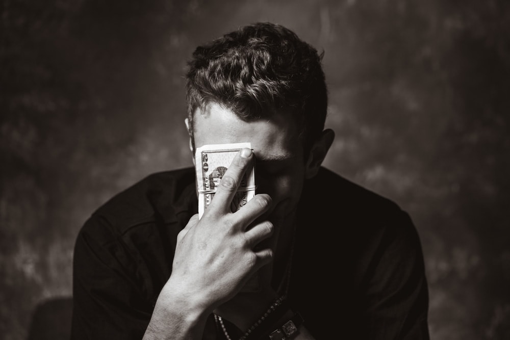 sitting man holding a stack of money to his face