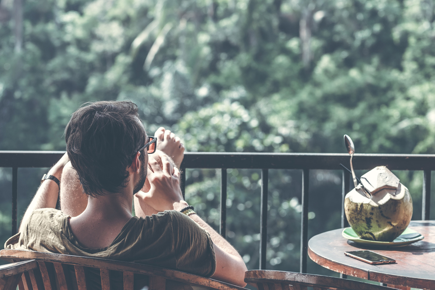 man in sunglasses sitting in a chair outside on a balcony next to table with coconut