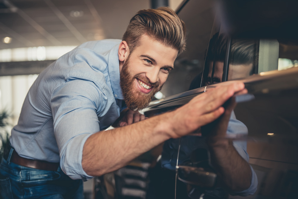 man smiling and touching a new car